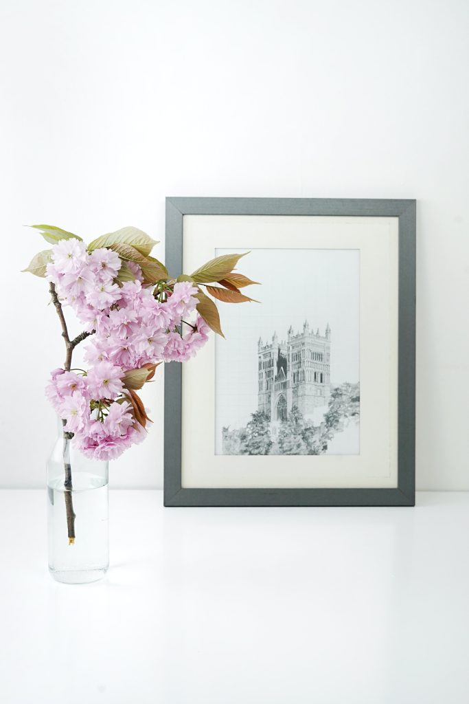 a sketch of a castle in a silver frame next to pink flowers in vase